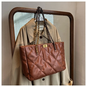 Detail of quilted brown tote bag with golden twist lock and metal chain strap