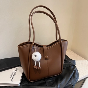 Brown leather bucket tote bag with plush charm and snap closure on dark leather surface