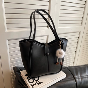 Black minimalist leather bucket bag with plush charm on stylish white display stand