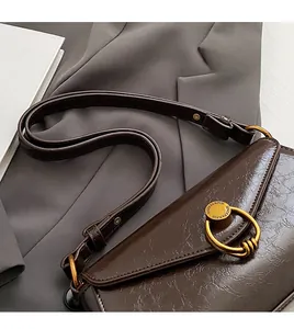 Detail of dark brown glossy patent leather shoulder bag with gold circular buckle