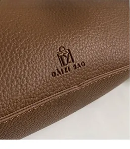 Close-up of litchi grain leather texture and embossed logo on brown shoulder bag
