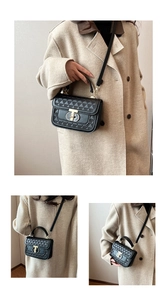 Detail of a black textured crossbody bag with a gold T-lock and adjustable shoulder strap