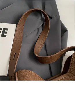 Close-up of smooth long shoulder strap on brown lychee texture leather bucket bag