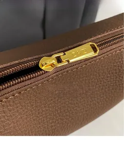 Close-up of golden zipper puller with logo on brown lychee grain leather bag detail