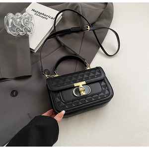 Detail of black quilted crossbody bag with gold T-lock on a stylish grey suit jacket
