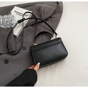 Detail of black leather crossbody bag with quilted flap and gold metal hardware on blazer