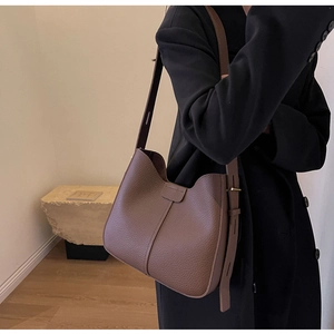 Detail of brown lychee grain leather bucket bag showing texture and saddle silhouette