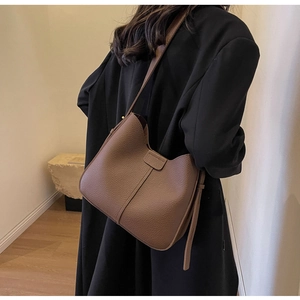 Detail of brown litchi pattern leather bucket bag shown on model with black blazer