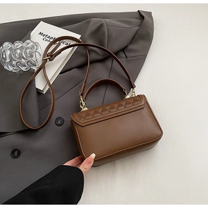 Detail of brown leather handbag with triangle embossing and adjustable strap on a gray blazer