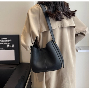 Close-up of a black lychee texture bucket bag worn with a classic beige trench coat