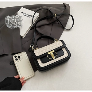 Detail of minimalist black and beige crossbody bag with golden T-lock on a grey blazer