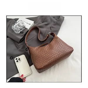Vista piatta di una borsa hobo intrecciata caramello con tracolla su abito grigio