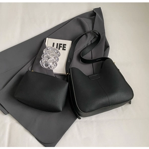Detail of black lychee texture leather bucket bag and matching pouch on suit fabric