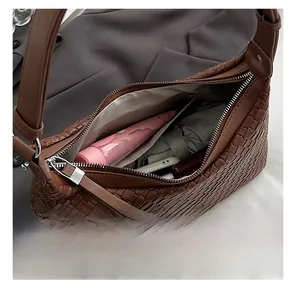 Dettaglio interno della borsa hobo intrecciata marrone scuro con oggetti comuni