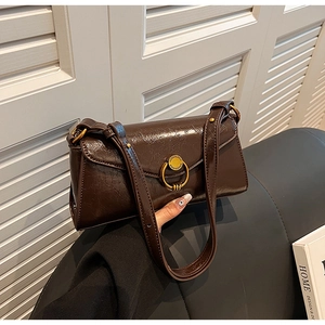 Detail of deep brown underarm bag showing oil wax leather texture and gold buckle
