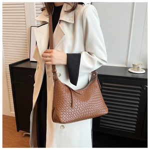 Borsa a spalla in pelle intrecciata marrone abbinata a un trench bianco in un interno