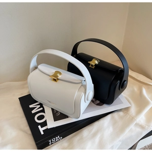 Close-up of white and black small square handbags featuring golden shell-shaped metal locks