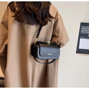 Chic black leather crossbody bag for women worn by model against a minimalist wall