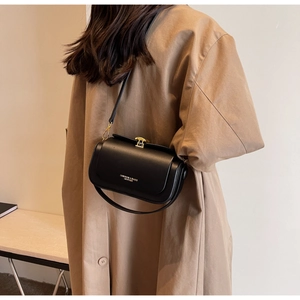 Detail of a black crossbody square bag with gold buckle on a model in a trench coat