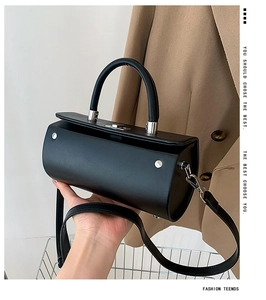 Détails d'un sac cylindrique noir avec boucle argentée et poignée en cuir lisse