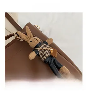 Detail of cute brown plush bunny charm with houndstooth vest and gold chain on tote bag