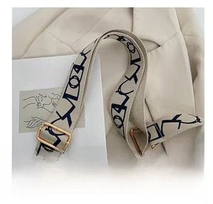 Detail of beige canvas wide strap with black geometric patterns and gold metal buckle