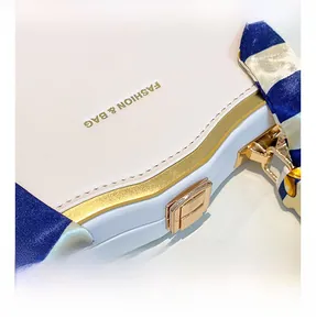 Detail of white leather box bag with gold metal hardware lock and striped silk scarf