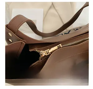 Detail view of smooth golden metal zipper and matte brown leather texture on tote bag