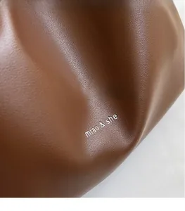 Detail of brown litchi pattern leather with silver miao & she logo on the shoulder bag