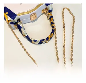 Detail of white box bag with gold metal trim and silk scarf wrapped top handle