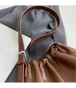 Detail of adjustable long shoulder strap and smooth leather pleats on brown bag