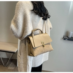 Detail of beige frosted leather handbag featuring a gold oval clasp and top handle