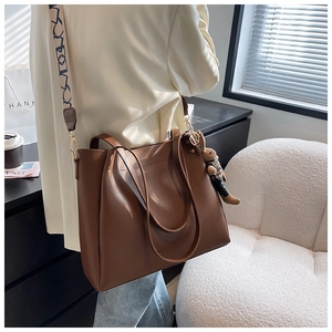 Detail of a brown leather tote bag with stylish patterned strap and plush bunny charm