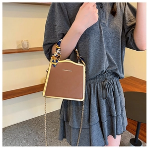 Brown box bag with silk scarf handle and gold chain strap shown on a model