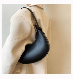 Detail of minimalist black leather crescent shoulder bag worn with a beige blazer