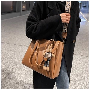 Brown tote bag detail with wide woven strap and cute rabbit pendant on model