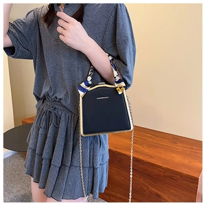 Detail of a black chain bag with silk scarf handle and golden metal frame detail