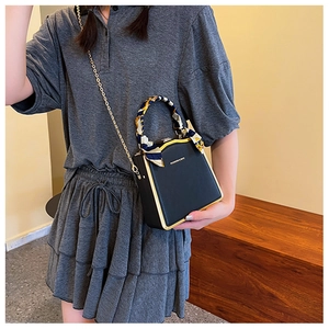 Detail of black box handbag with gold frame and decorative printed silk scarf on handle