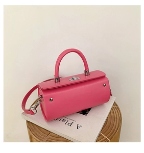 Vue détaillée d'un sac boîte cylindrique rose vif avec finitions argentées sur un tabouret