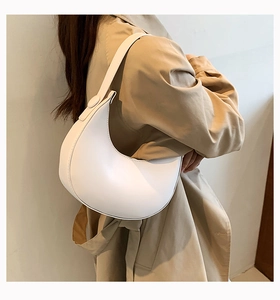 Minimalist white half-moon shoulder bag shown from a side view with neutral trench coat