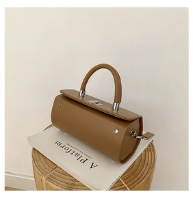 Détail d'un sac cylindrique marron avec fermoir argenté et poignée sur décor épuré