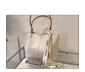 Close-up of a large beige tote bag featuring decorative branded ribbons and brown handles