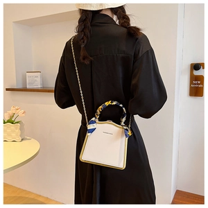 Chic white box bag with silk scarf wrapped handle and gold chain strap on a model