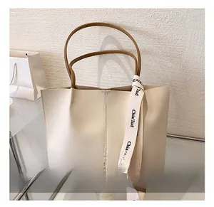 Detail view of large beige tote bag with brown handles and decorative ribbon accent