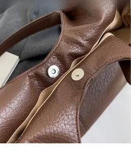 Detail of magnetic snap closure on brown faux leather tote with pebble grain texture