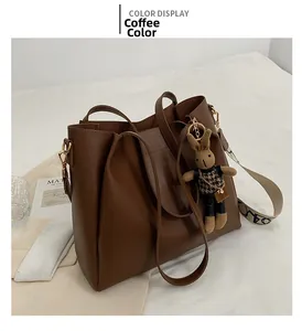 Detail view of large brown tote bag with plush bunny charm and wide logo strap