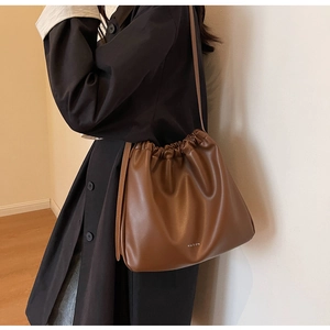 Detail view of a brown soft leather drawstring bag with brand logo and slim shoulder strap