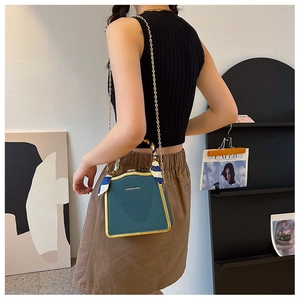 Detail view of dark green box bag with gold trim, chain strap and silk scarf handle decor