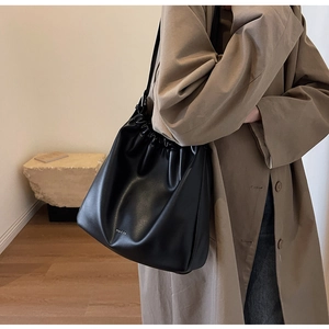Detail of a black leather drawstring bucket bag featuring a white logo and soft folds
