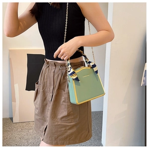 Detail of mint green box bag with gold metal frame and silk scarf handle on model
